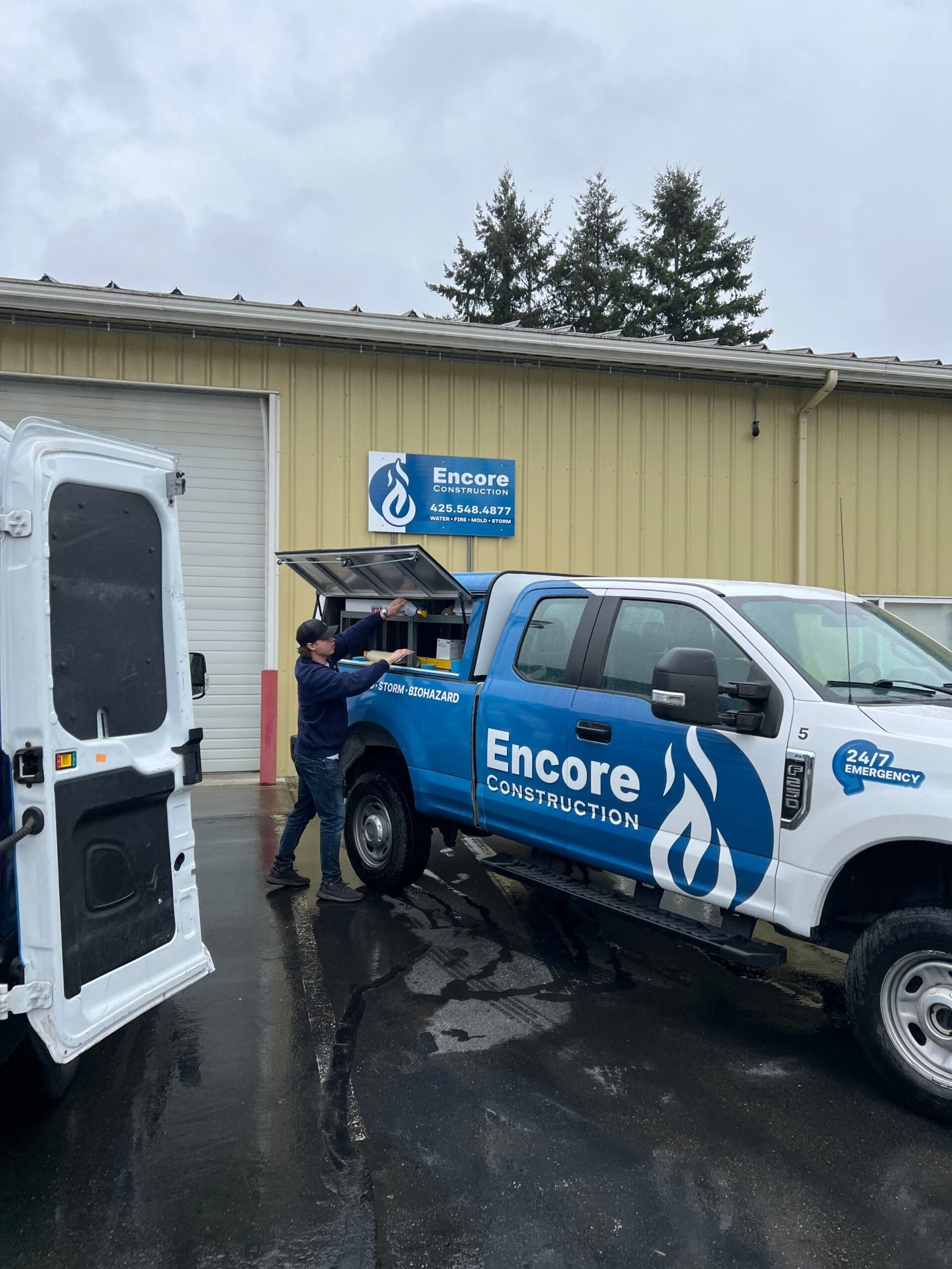 Two workers beside an Encore Construction pickup and cargo van