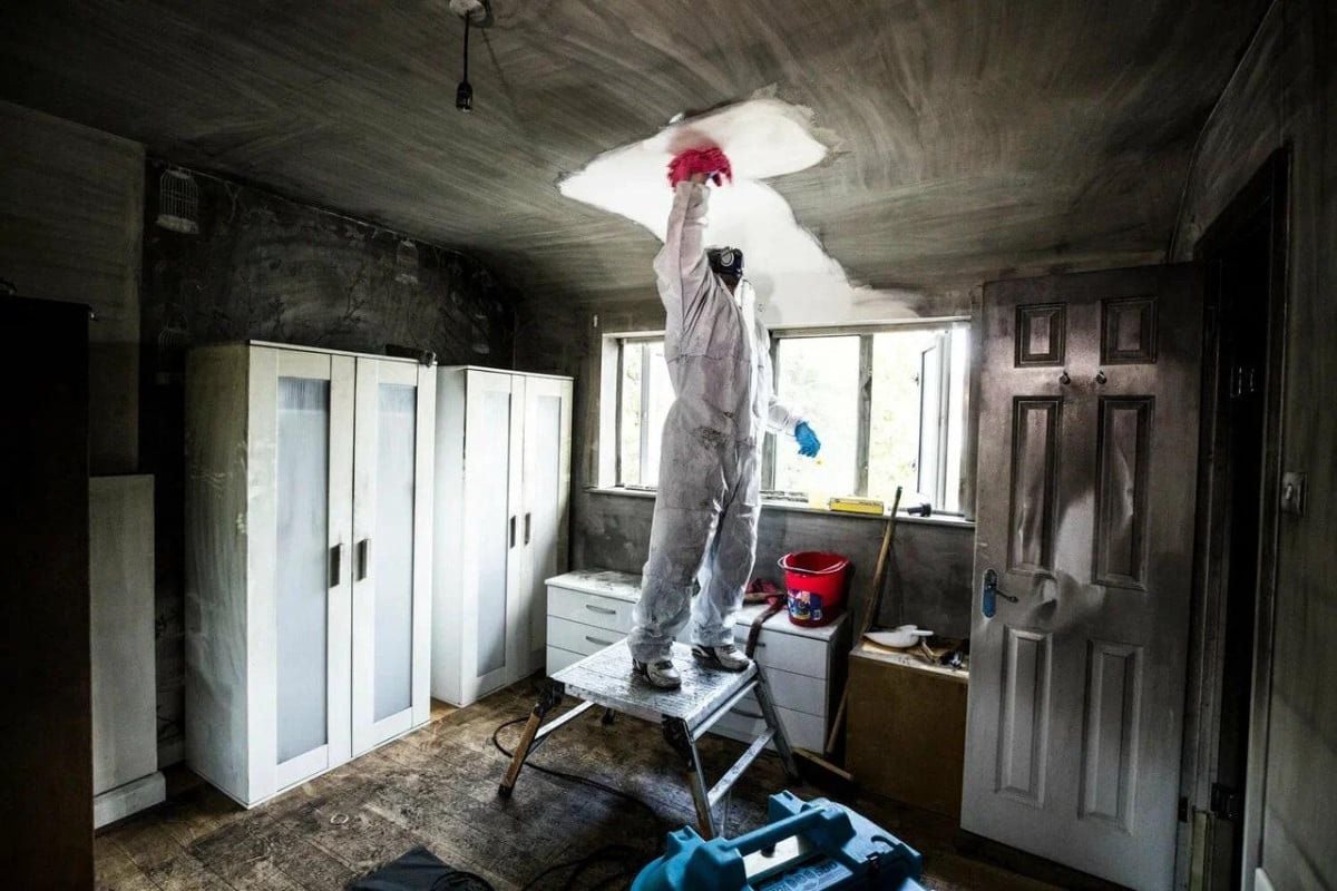 Restoration technician cleaning soot from a fire-damaged ceiling