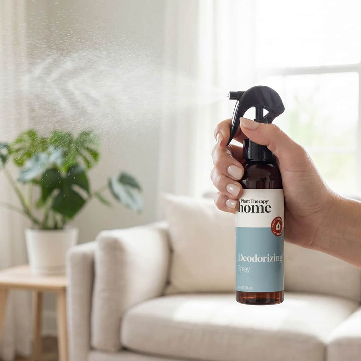 Hand applying deodorizing spray beside upholstered furniture