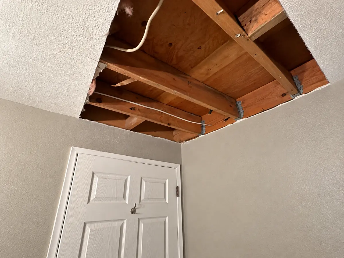 Ceiling opened to expose wood joists and electrical wiring during interior repair work.